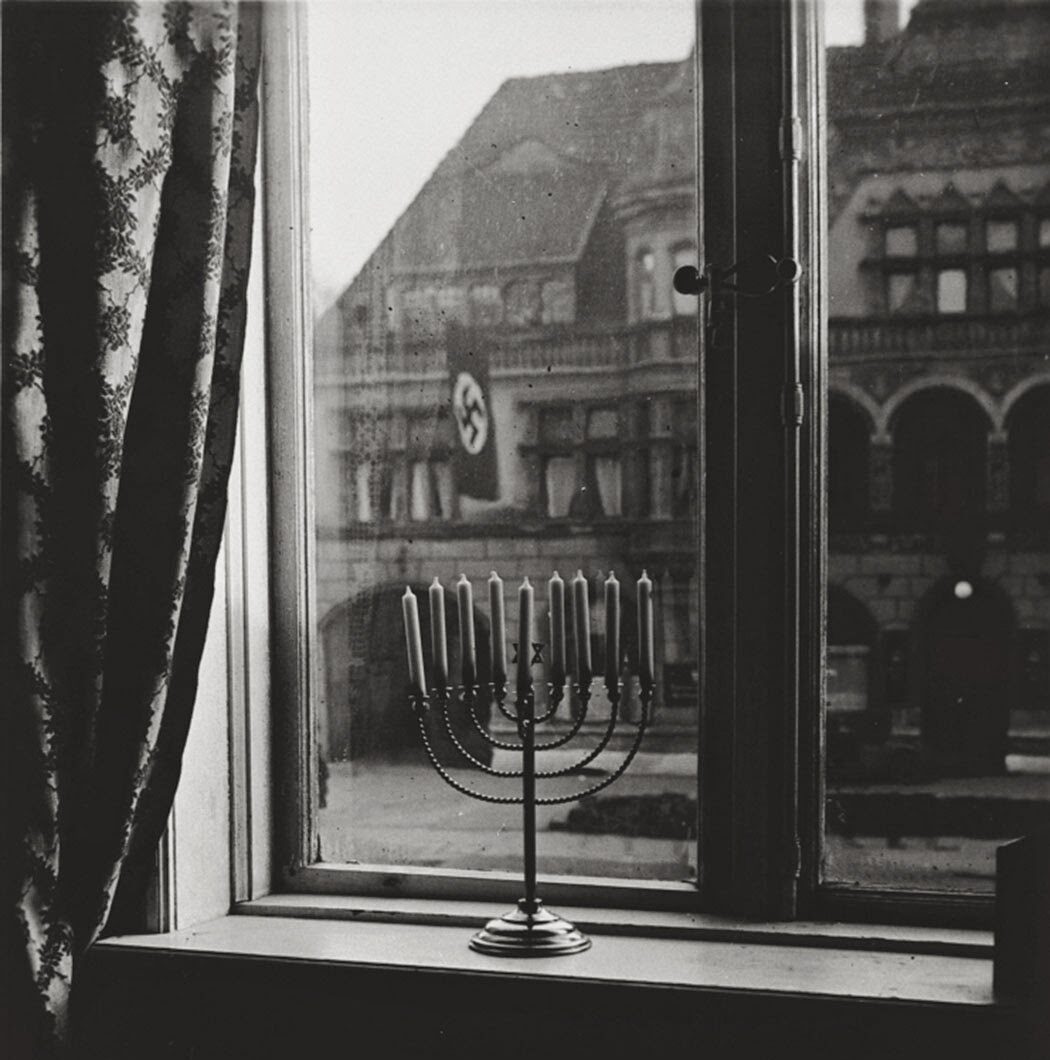 Photograph of a memorah in a window. A Nazi flag flies outside, 1931.